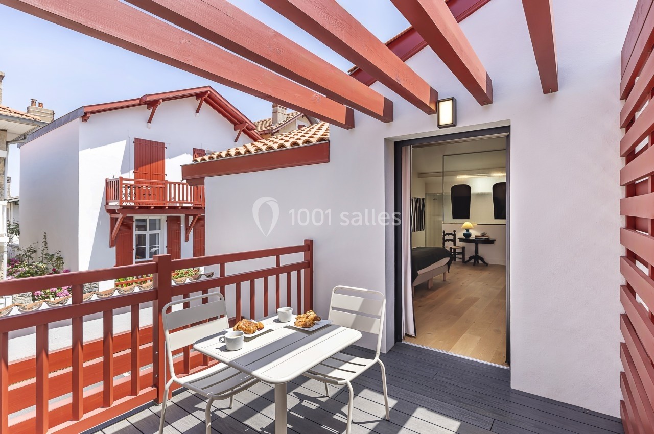 Balcon avec table et chaises, petit-déjeuner servi, vue sur des maisons blanches et rouges sous un ciel dégagé.