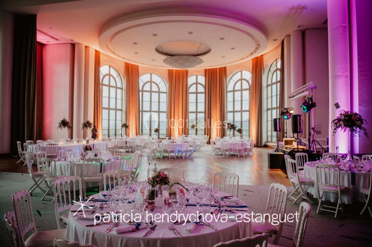 Salle de réception élégante avec tables rondes décorées, grandes baies vitrées et éclairage coloré.