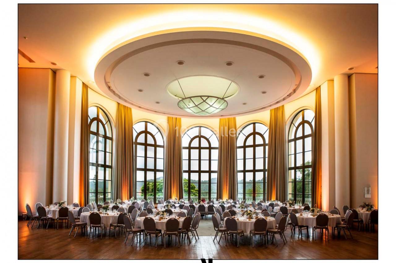 Salle de réception élégante avec de grandes baies vitrées, tables rondes dressées et éclairage chaleureux.
