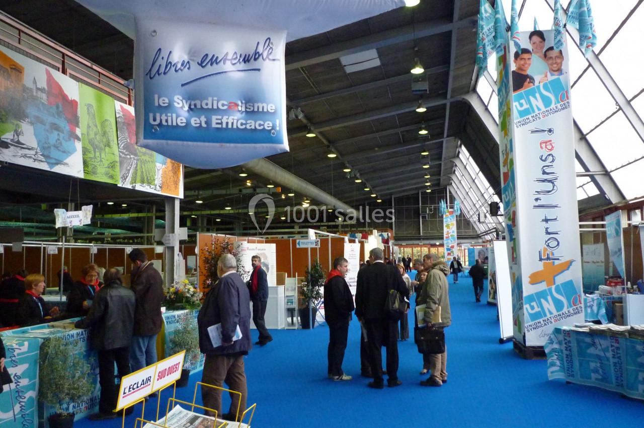 Des visiteurs circulent dans une allée d'un salon professionnel avec des stands et des affiches promotionnelles.