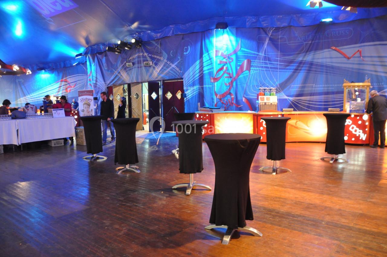 Salle aménagée avec des tables hautes noires, un comptoir éclairé et des décorations lumineuses sur les murs.