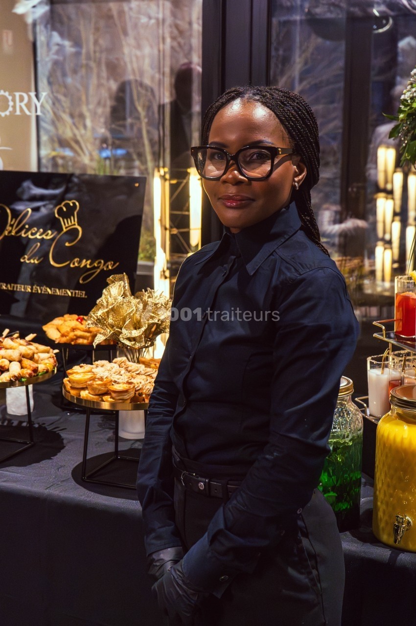 Une femme en tenue professionnelle se tient devant une table garnie de plats et de boissons lors d'un événement.