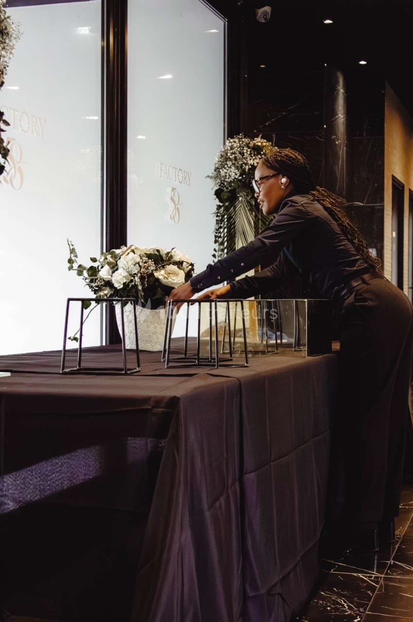Une femme disposant des fleurs sur une table recouverte d'une nappe noire dans un espace intérieur élégant.
