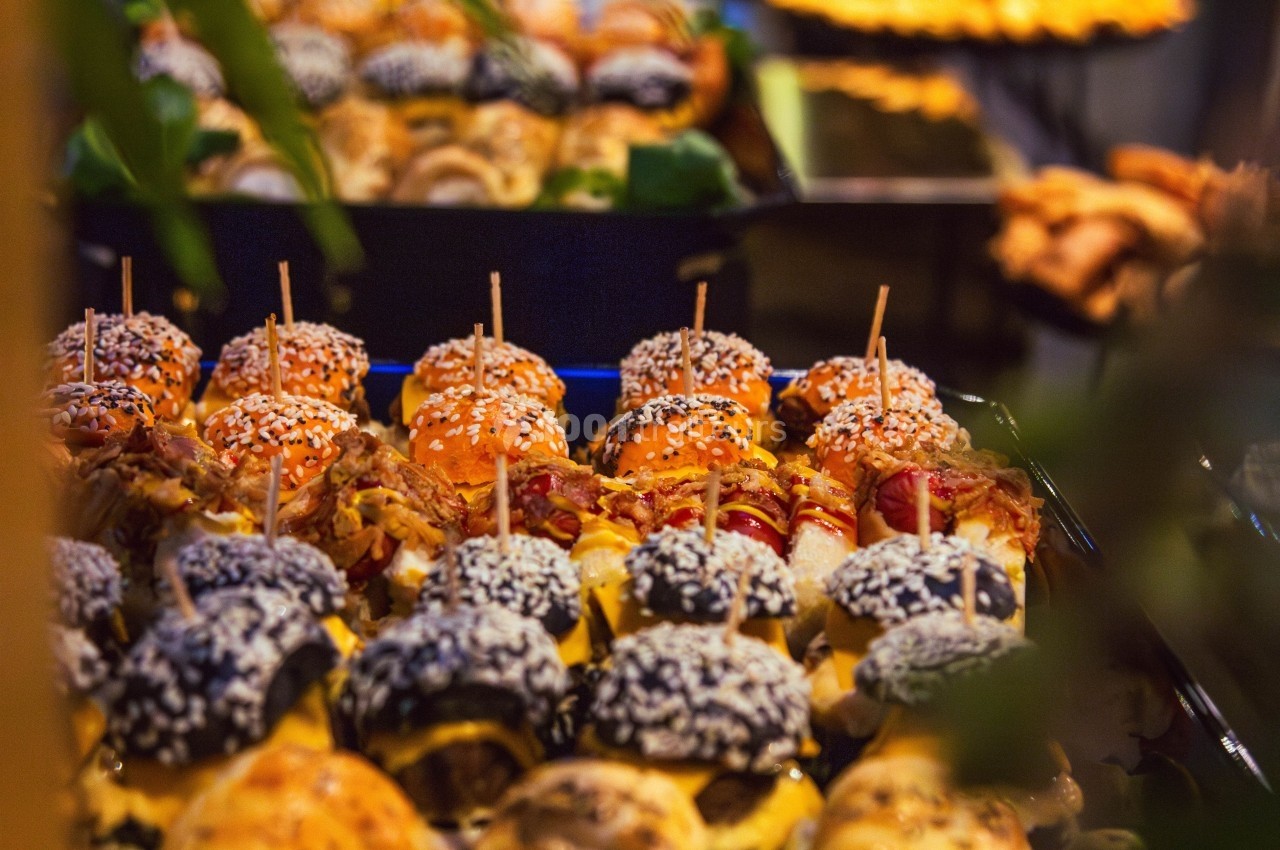 Plateau de mini-burgers variés garnis de graines de sésame, disposés sur une table lors d'un buffet.