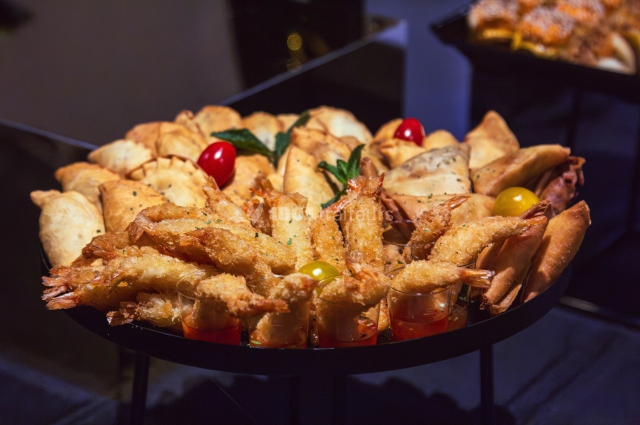 Plateau de bouchées apéritives comprenant crevettes panées, samoussas et feuilletés, présenté sur une table.