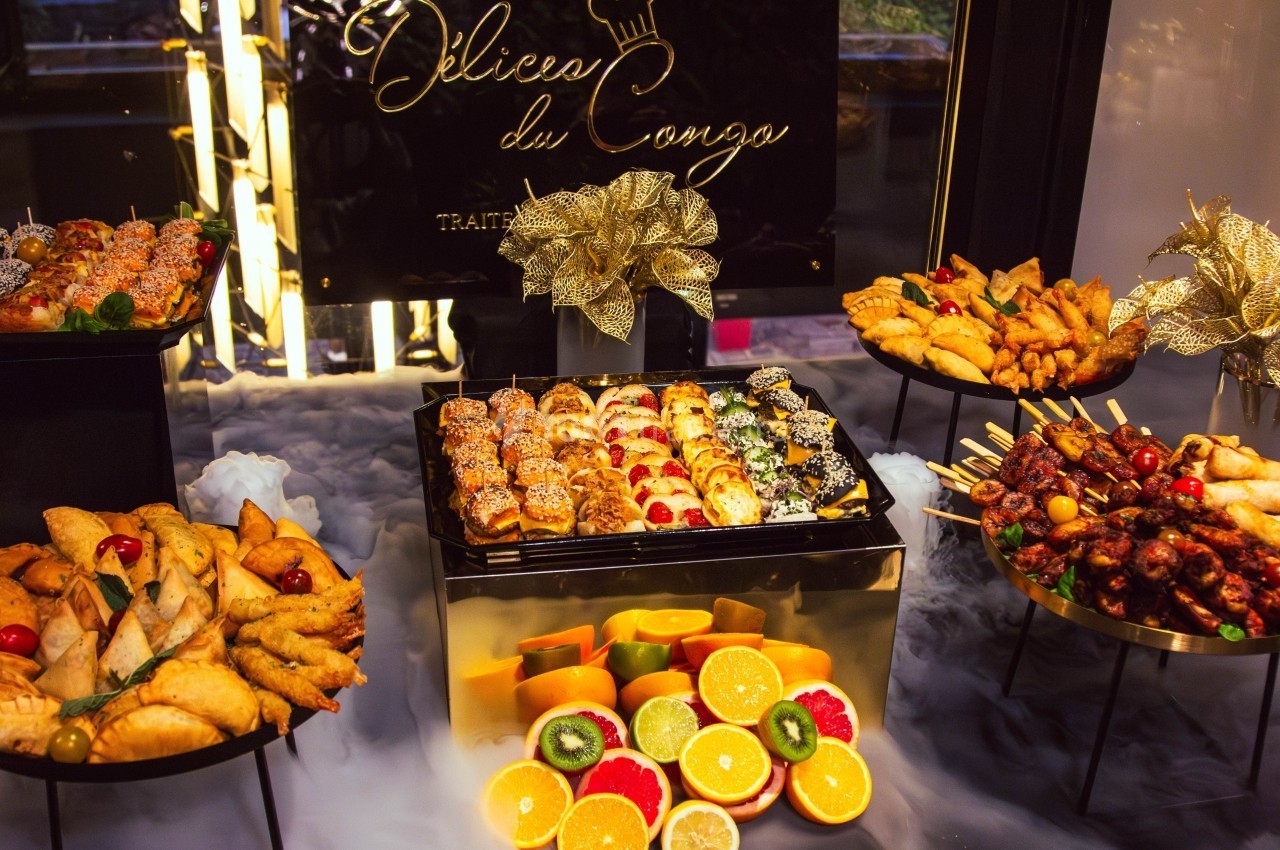 Plateau de buffet varié avec sushis, fruits frais, brochettes et assortiments de beignets, décoré de motifs dorés.