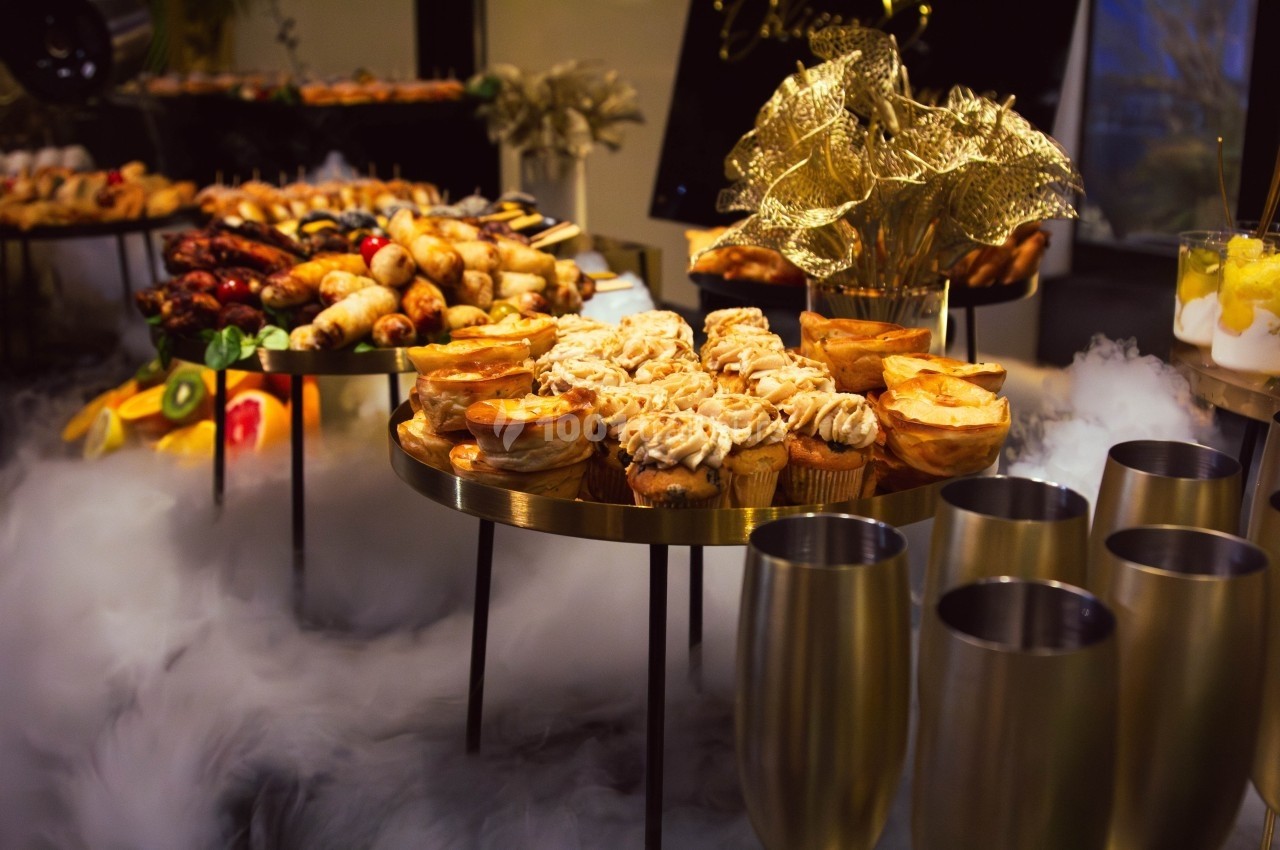 Buffet élégant avec desserts variés, fruits et décorations dorées, entouré d'une légère brume.
