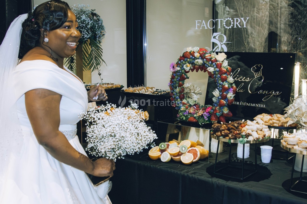 Une mariée souriante en robe blanche devant une table garnie de desserts et de décorations colorées.
