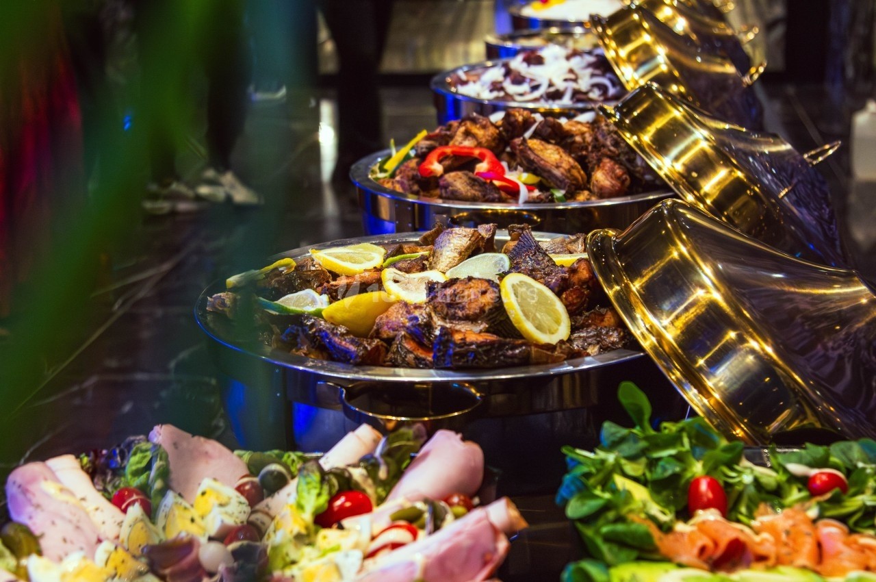 Buffet avec plats variés, incluant viandes grillées garnies de citron et légumes frais en présentation colorée.