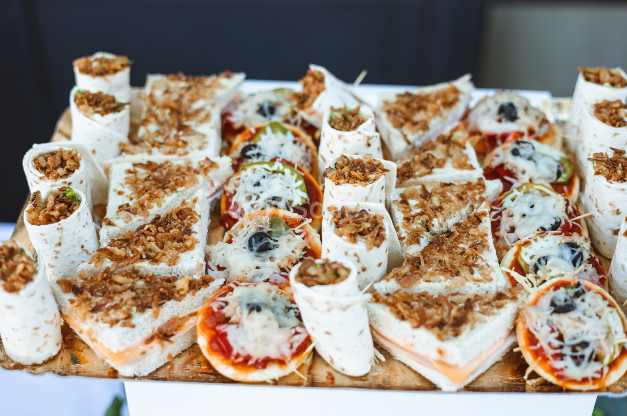 Plateau de wraps et mini-pizzas garnis de fromage râpé et d'oignons frits, présenté sur une planche en bois.