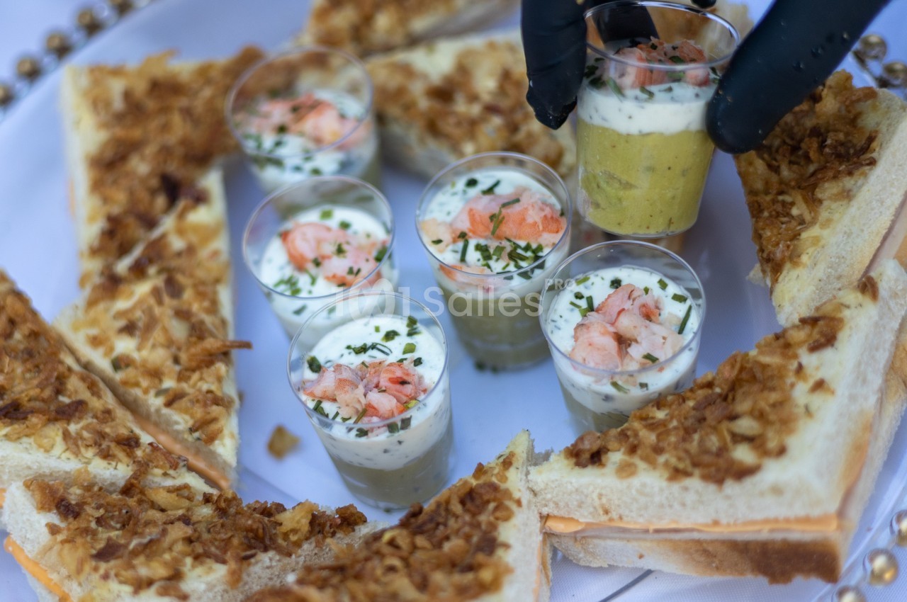 Verrines garnies de crevettes et herbes fraîches entourées de triangles de pain toasté avec oignons frits.