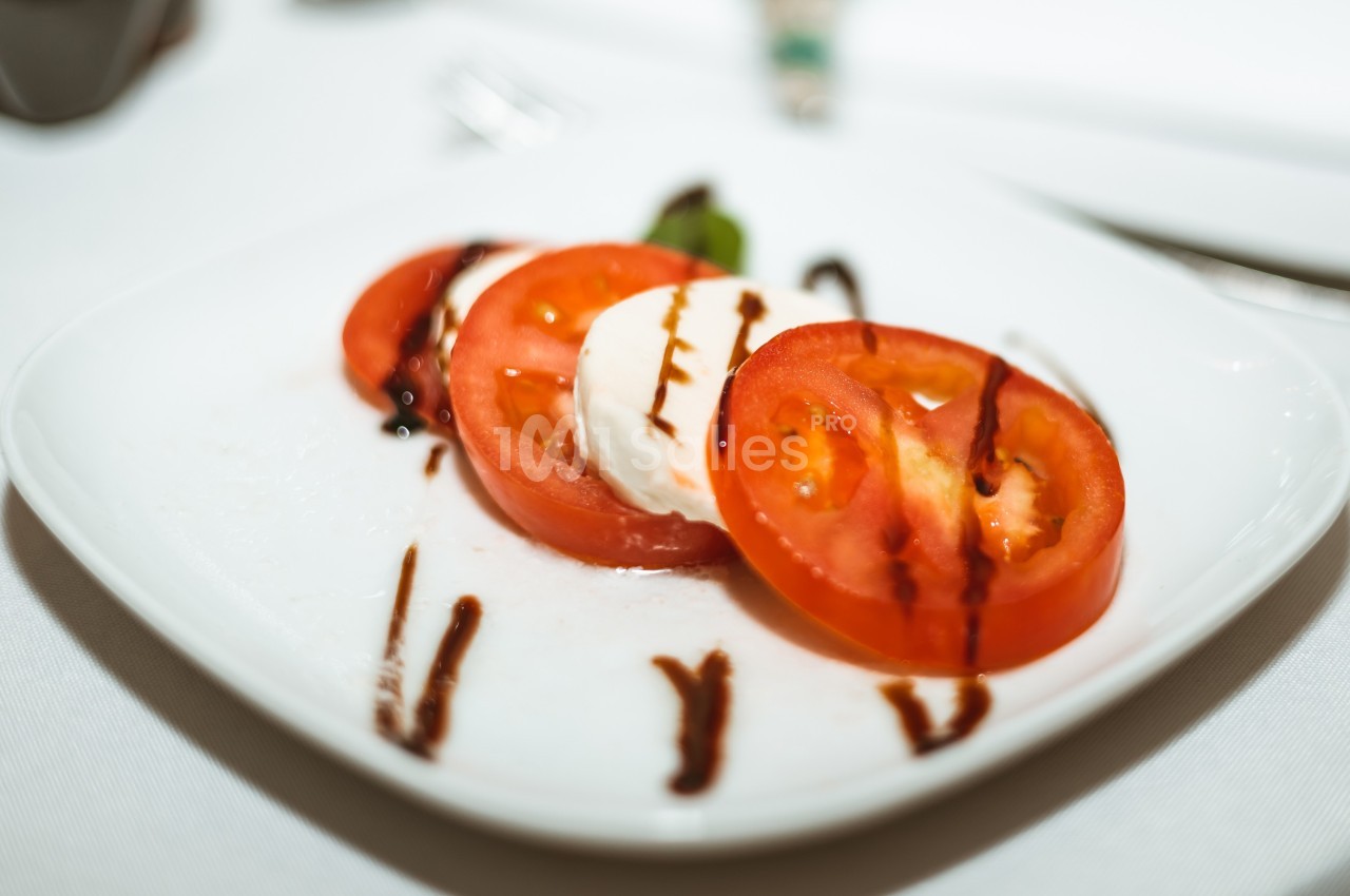 Tranches de tomate et mozzarella garnies de filet de vinaigre balsamique sur une assiette blanche.