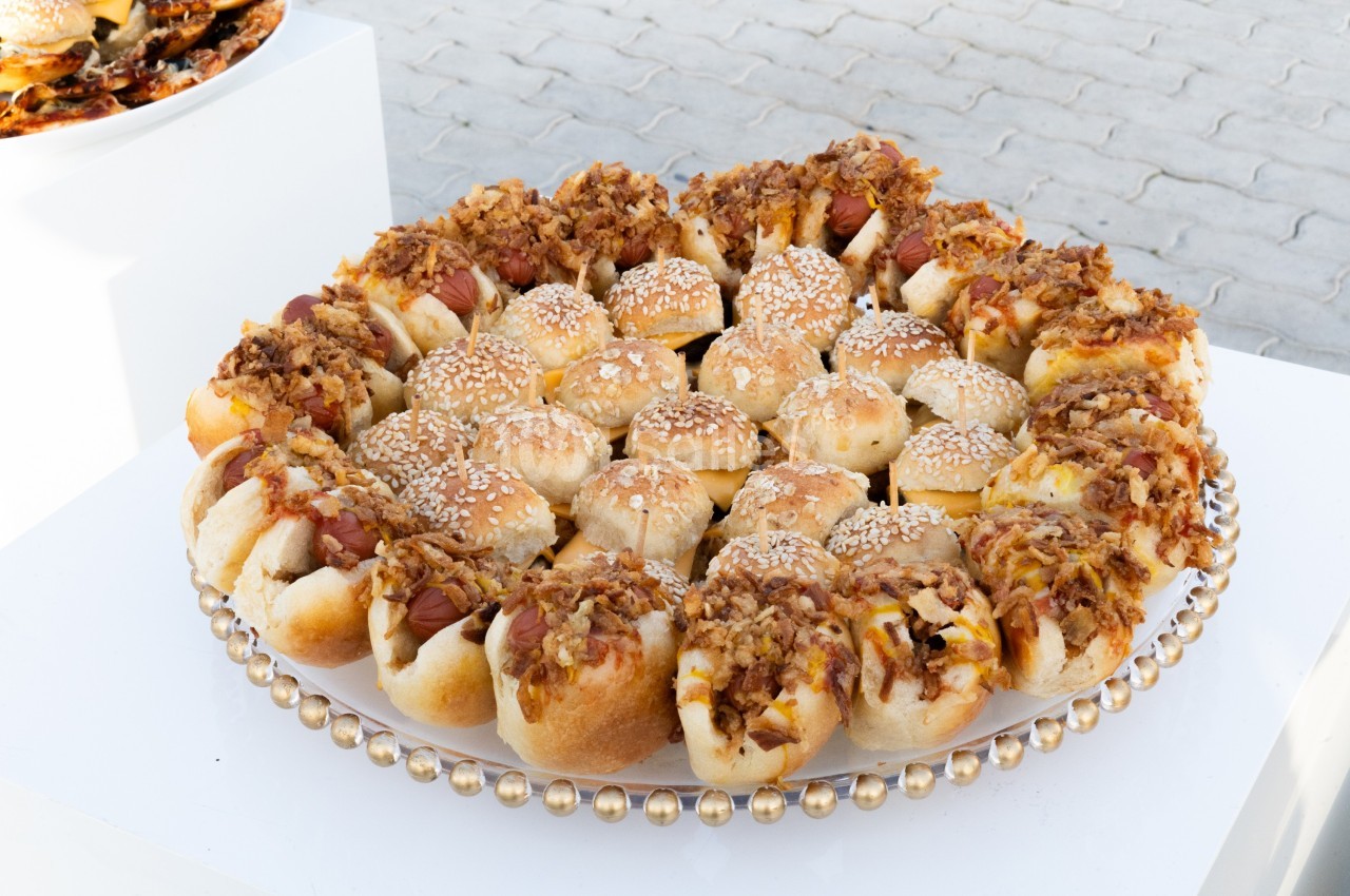 Plateau circulaire de petits pains garnis de saucisses, fromage, oignons caramélisés et graines de sésame.