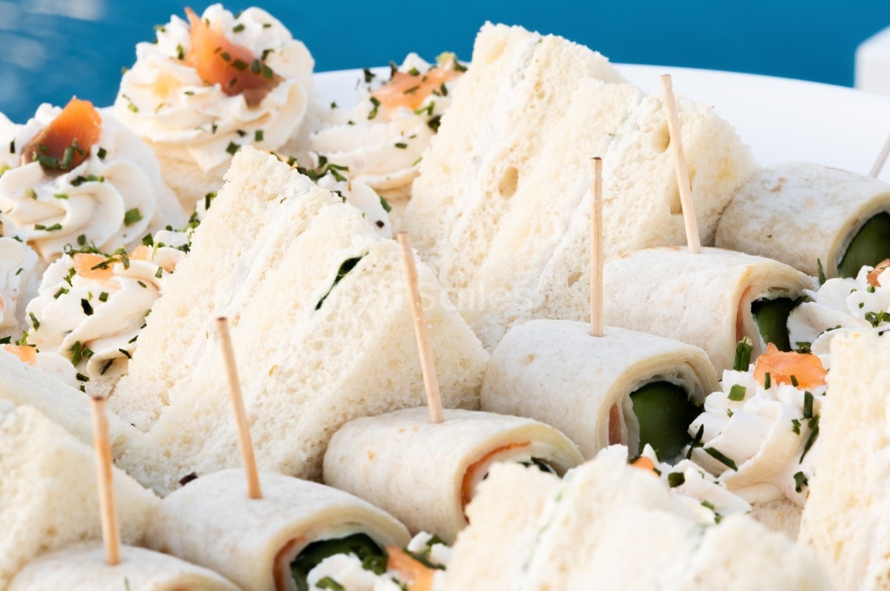 Assortiment de sandwichs roulés et triangles garnis, présentés sur un plateau avec décorations de crème et ciboulette.