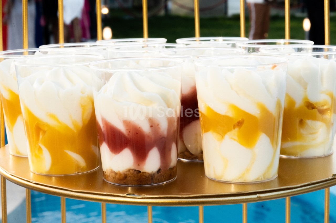 Desserts en verrines avec mousse blanche, coulis de mangue et de fruits rouges, présentés sur un plateau doré.