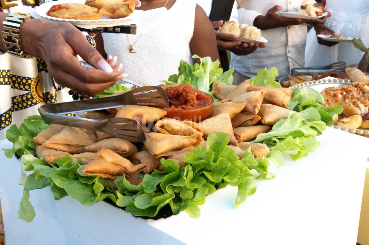 Assortiment de samoussas disposés sur un lit de salade verte, accompagnés d'une sauce rouge au centre.