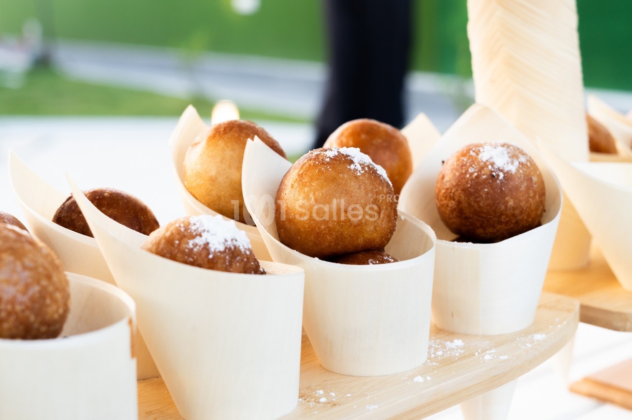 Beignets dorés saupoudrés de sucre glace, présentés dans des cônes en bois sur un présentoir.