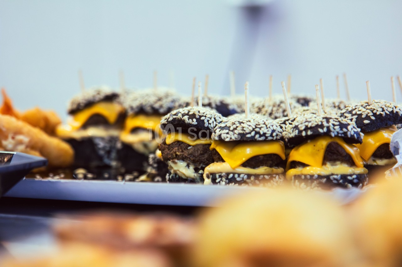 Burgers au pain noir garnis de fromage fondu et de graines de sésame, présentés sur un plateau.