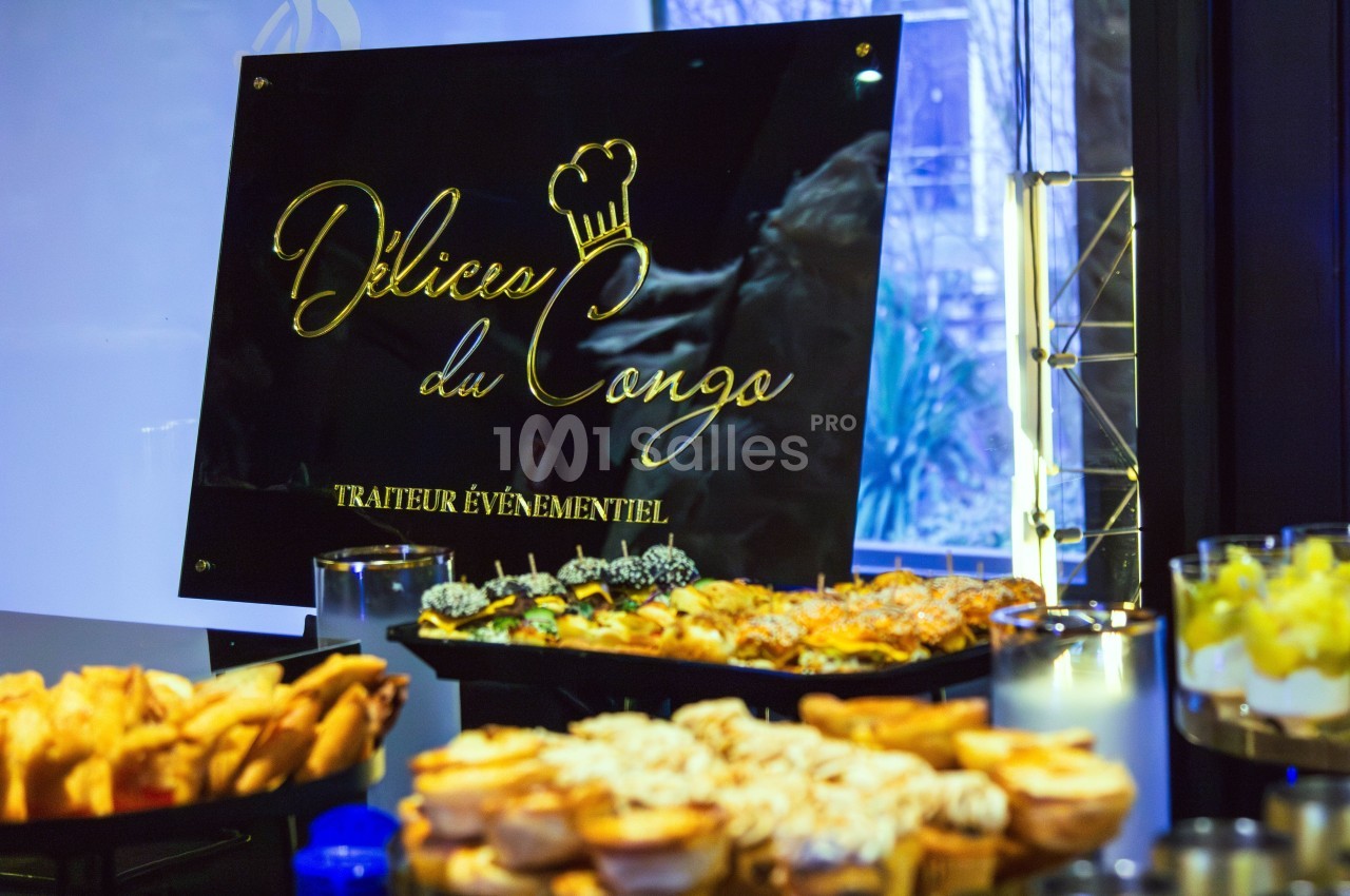 Buffet varié avec des plats salés et sucrés devant un panneau ’Délices du Congo, traiteur événementiel’.