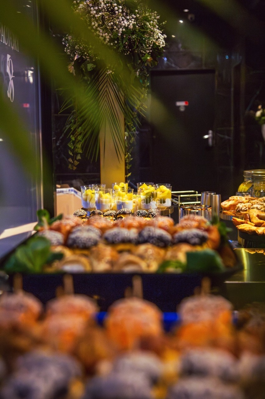 Plateau de pâtisseries variées au premier plan avec des verrines de desserts en arrière-plan dans un cadre élégant.