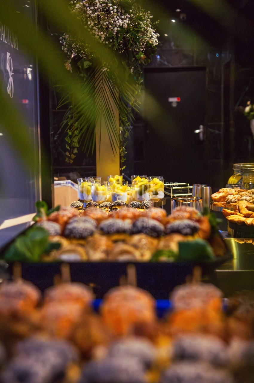 Plateau de pâtisseries variées au premier plan avec des verrines de desserts en arrière-plan dans un cadre élégant.