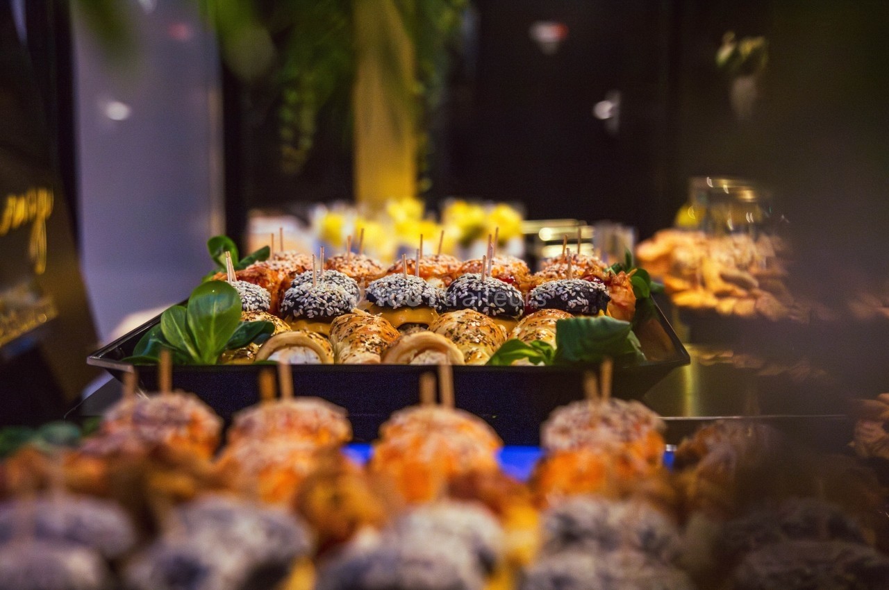 Plateau de mini-burgers variés garnis de graines et légumes, présentés sur une table dans un cadre lumineux.