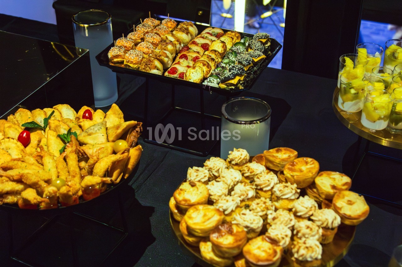 Plateaux de petits fours salés et sucrés disposés sur une table noire lors d'un buffet.