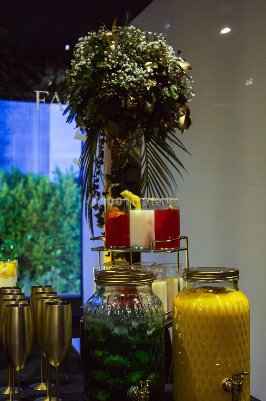 Buffet avec boissons colorées en carafes, verres dorés et une décoration florale en arrière-plan.