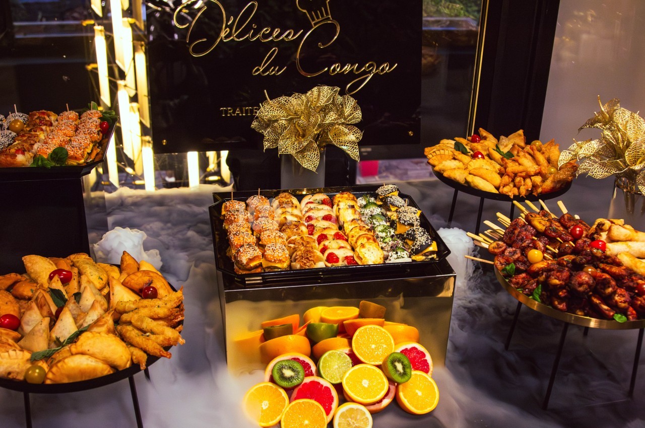 Plateau de buffet avec sushis, fruits frais, brochettes et assortiments de beignets, décoré de motifs dorés.