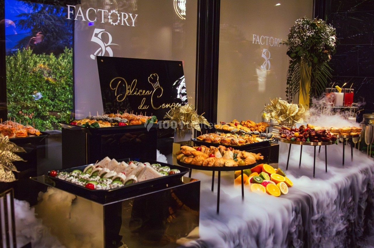 Buffet élégant avec plats variés, fruits et décorations, entouré d'effets de fumée et d'un panneau ’Délices du Chef’.