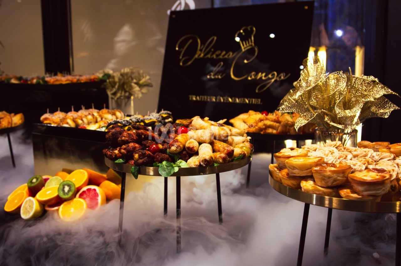 Buffet élégant avec divers plats et amuse-bouches, entouré de fumée décorative et d'un panneau en arrière-plan.