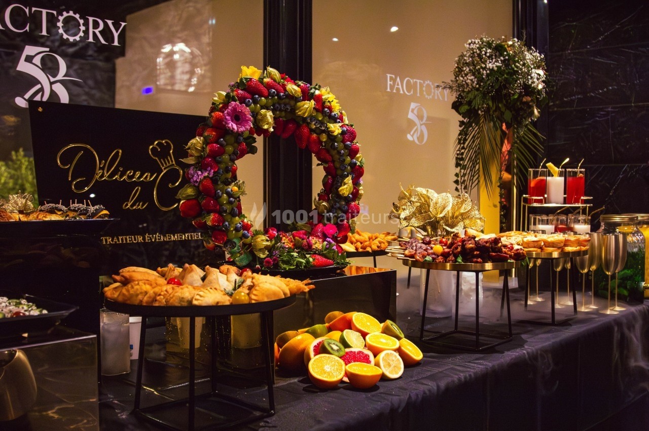 Table garnie de plats variés, fruits frais et décorations florales dans un cadre élégant et lumineux.