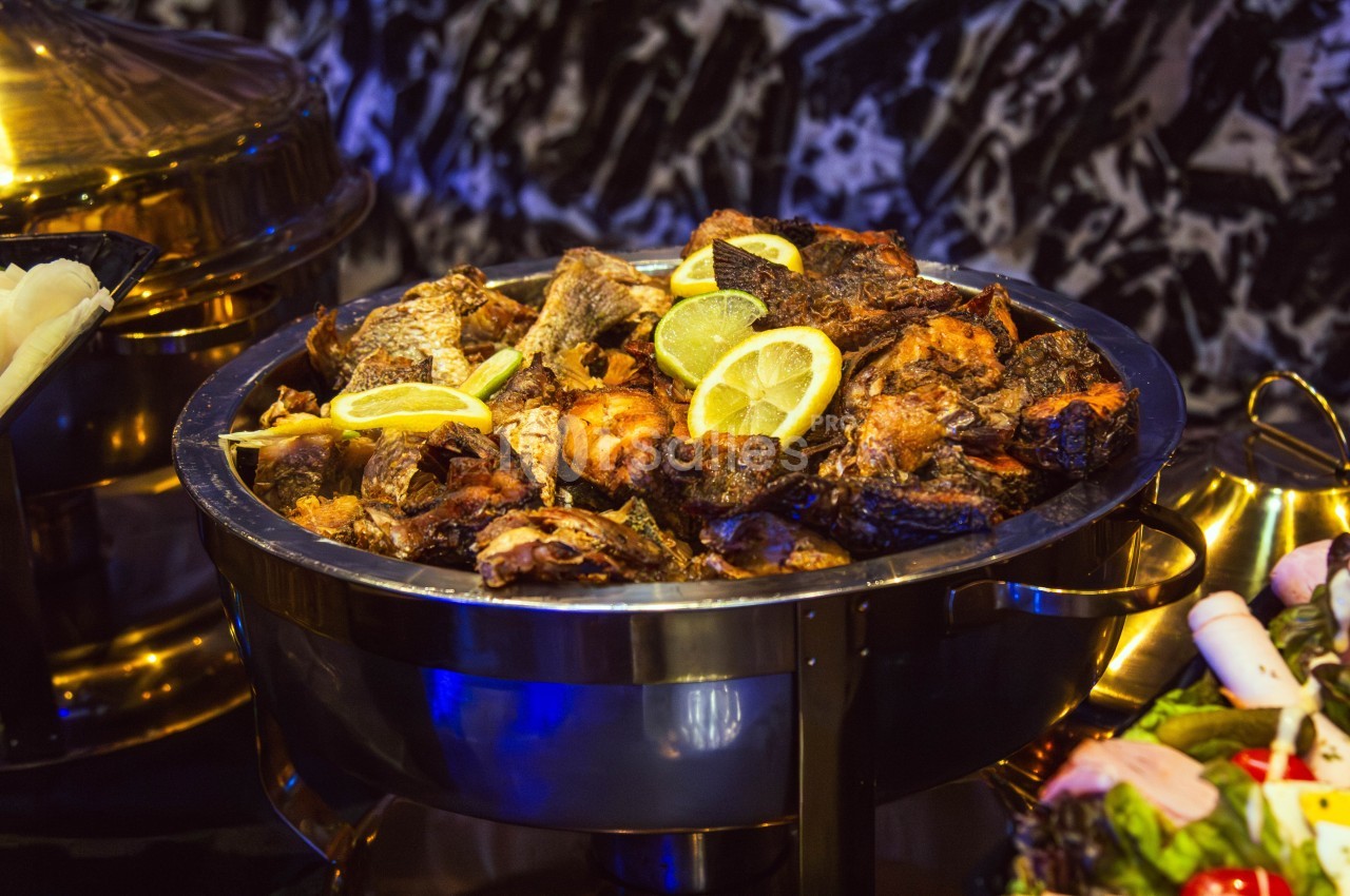 Plat de poissons frits garnis de tranches de citron, présenté dans un récipient en métal sur une table.