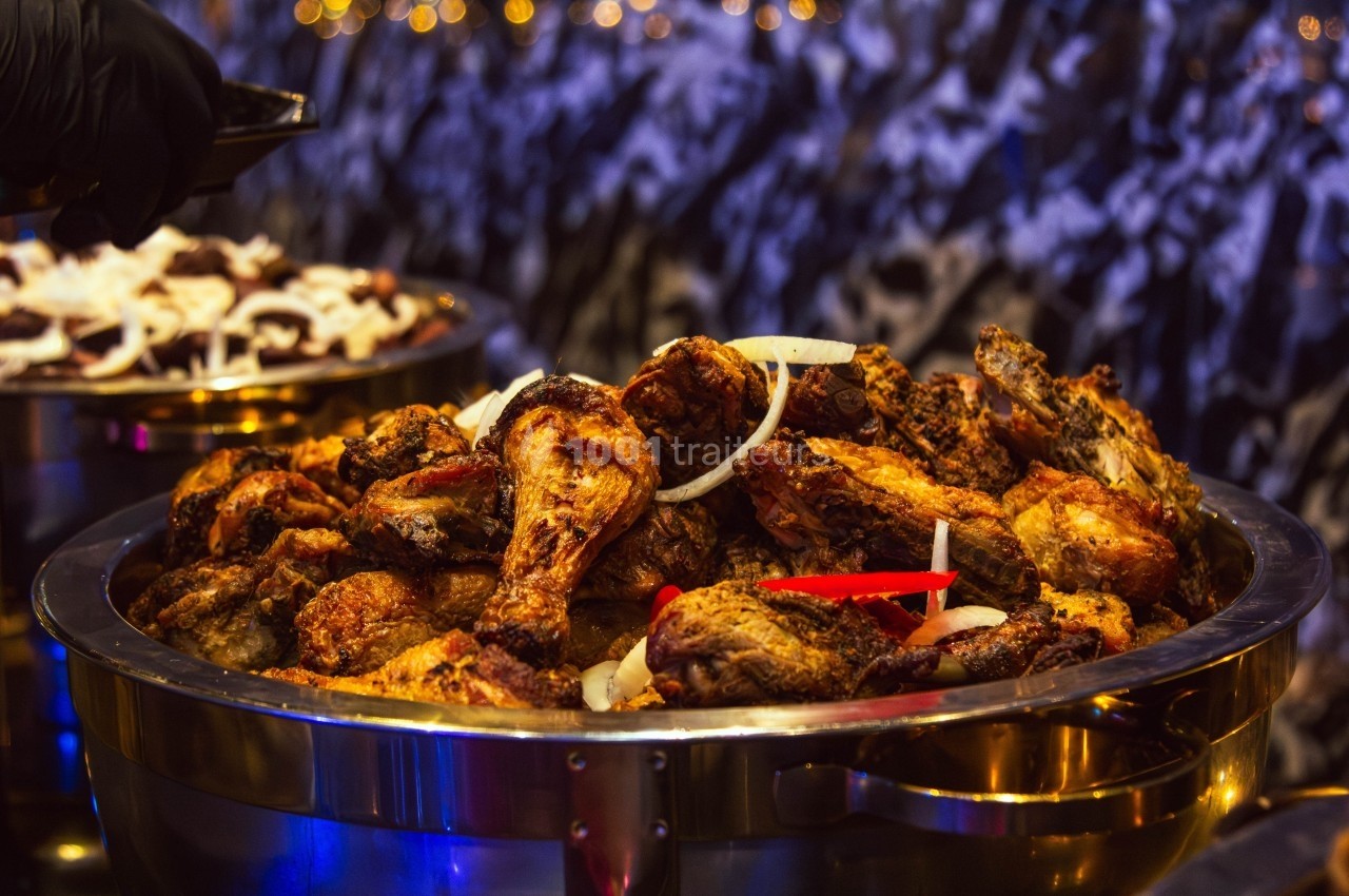 Poulet rôti épicé servi dans un plat en métal, garni de rondelles d'oignon et de morceaux de piment rouge.