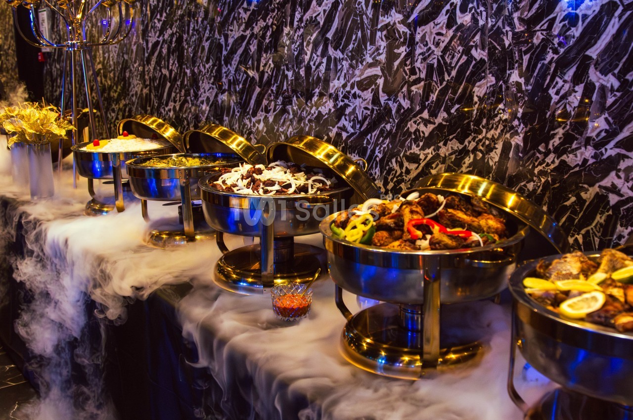 Buffet avec plusieurs plats chauds présentés dans des récipients en métal, entourés de vapeur décorative.