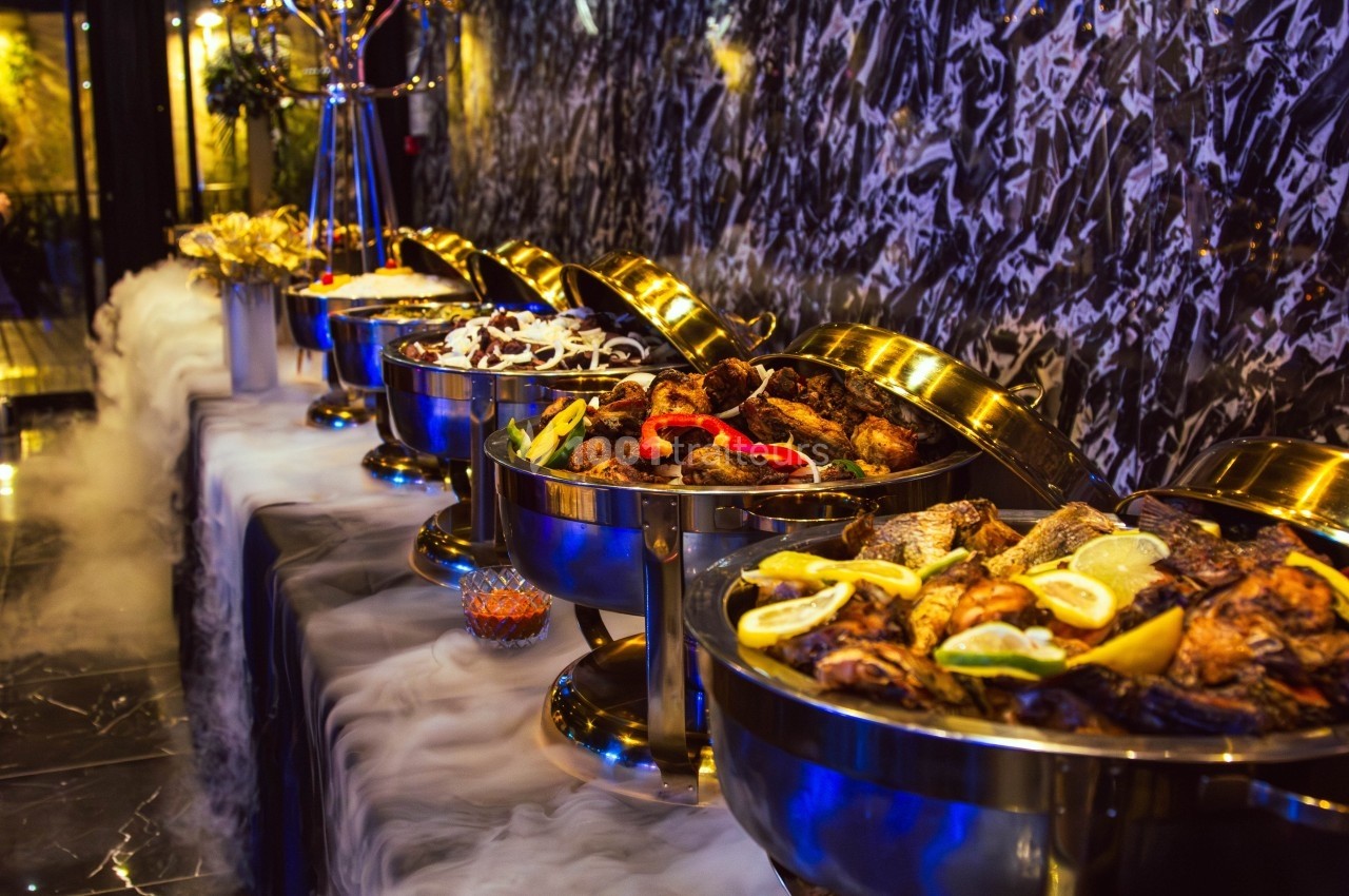 Buffet de plats variés présentés dans des récipients en métal, avec une décoration élégante et un effet de fumée.