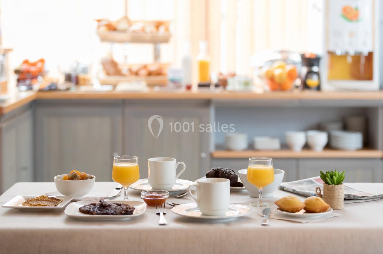 Petit-déjeuner servi sur une table avec viennoiseries, boissons chaudes, jus d'orange et confitures.