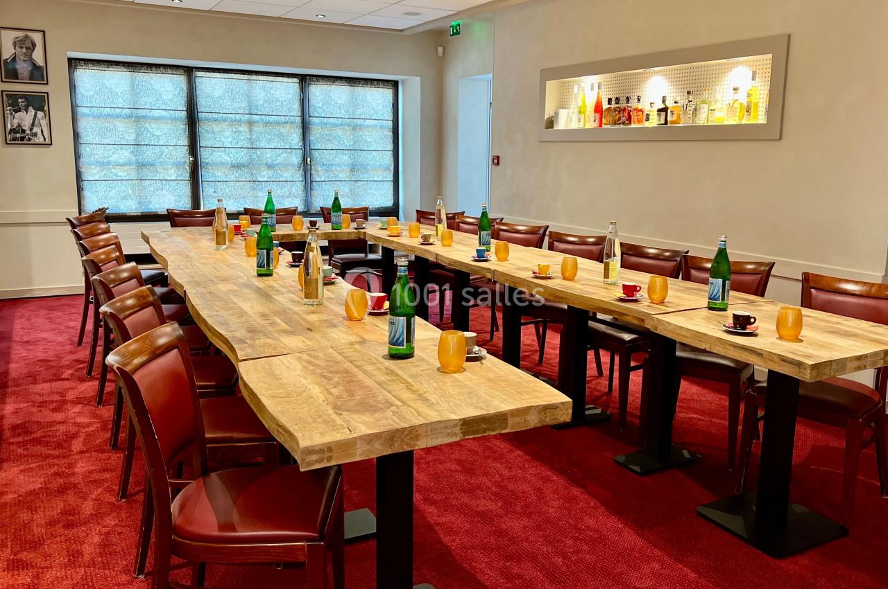 Salle de réunion avec tables en bois disposées en U, chaises en bois, bouteilles d'eau et tasses sur les tables.