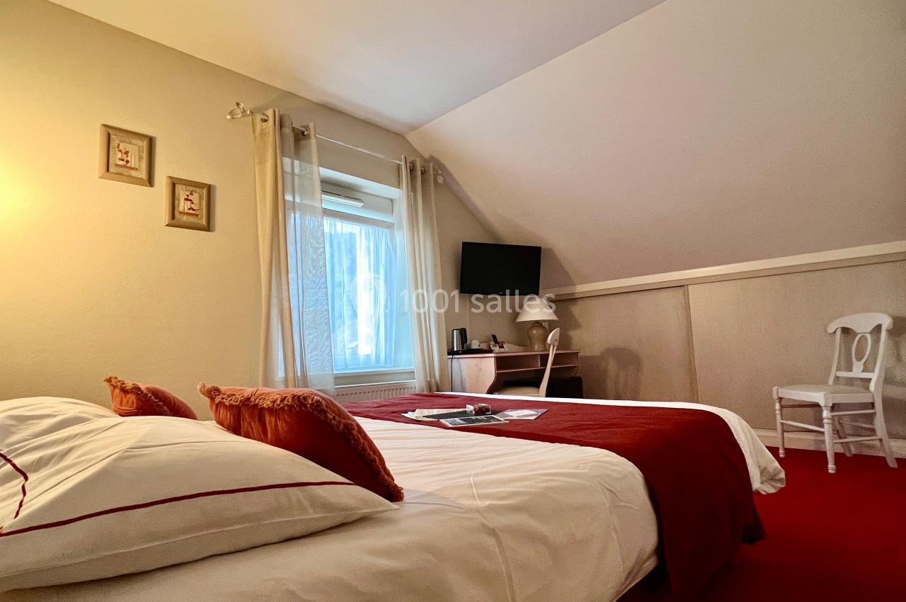 Chambre lumineuse avec lit double, draps blancs et rouges, bureau, chaise, télévision et fenêtre donnant sur l'extérieur.