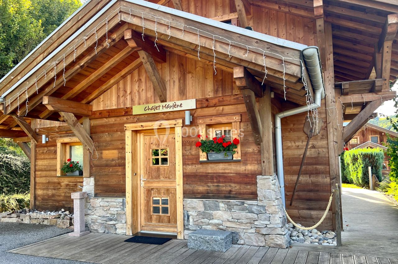 Chalet en bois avec jardinières fleuries, toit incliné et chemin en bois, entouré de verdure.