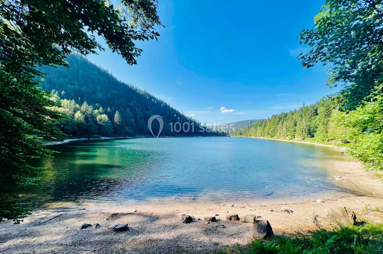 Vue d'un lac entouré de forêts et de montagnes sous un ciel bleu dégagé.