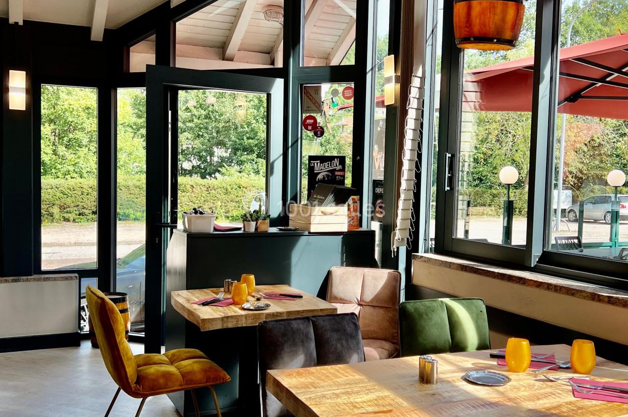Salle de restaurant lumineuse avec tables dressées, chaises colorées et vue sur une terrasse extérieure ensoleillée.