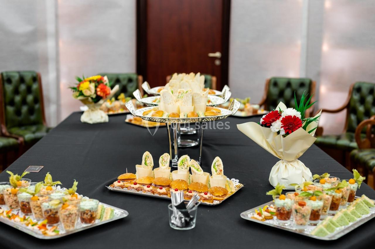 Buffet avec des amuse-bouches variés, disposés sur des plateaux élégants dans une salle avec des chaises en arrière-plan.