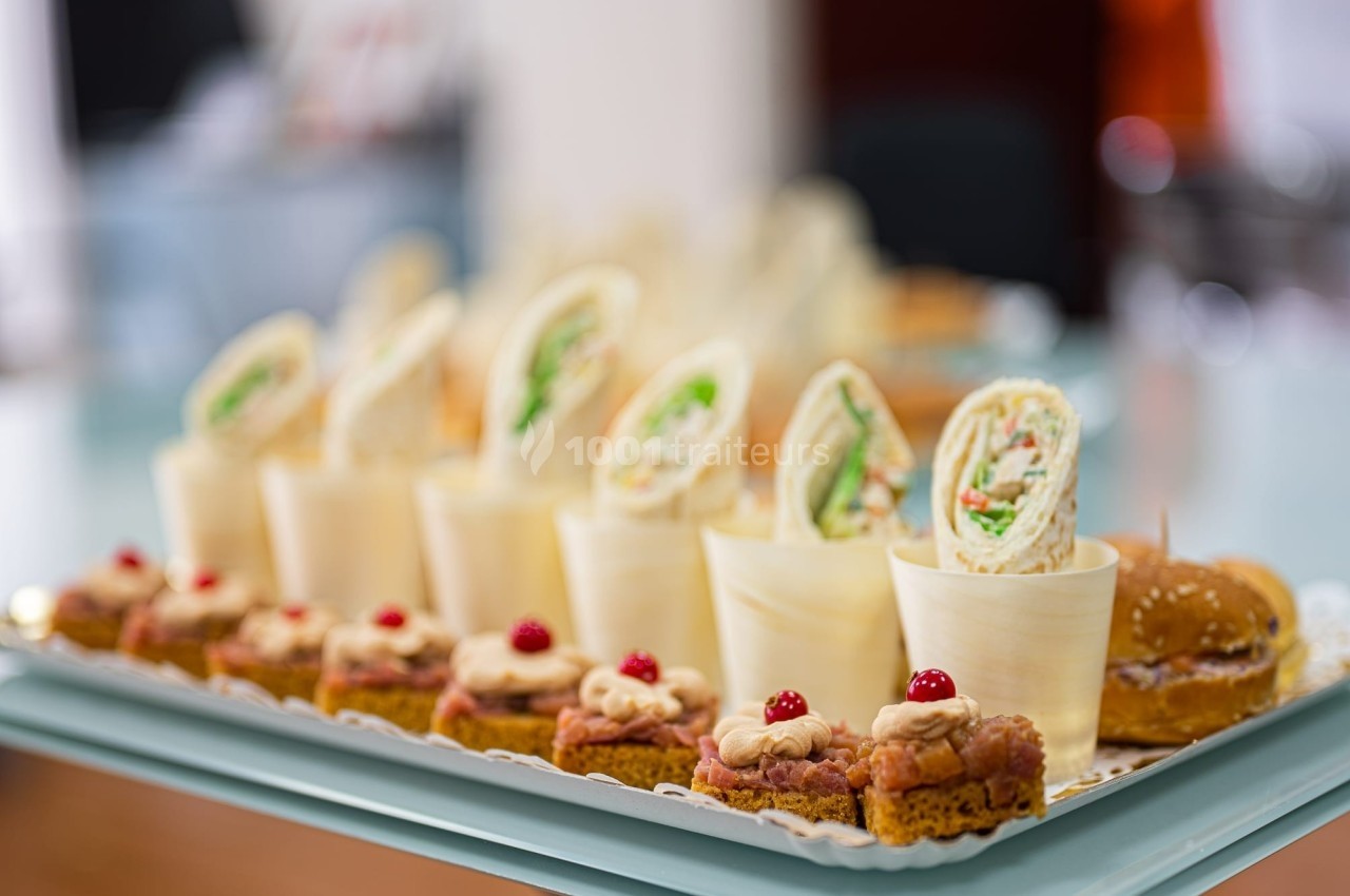 Plateau de bouchées apéritives variées comprenant wraps, mini-gâteaux et petits pains garnis.