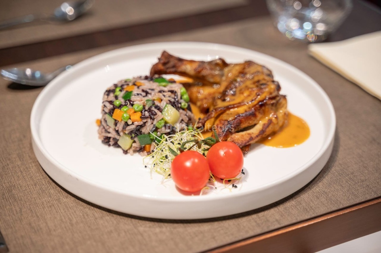 Assiette contenant des morceaux de viande en sauce, un mélange de riz aux légumes et deux tomates cerises.