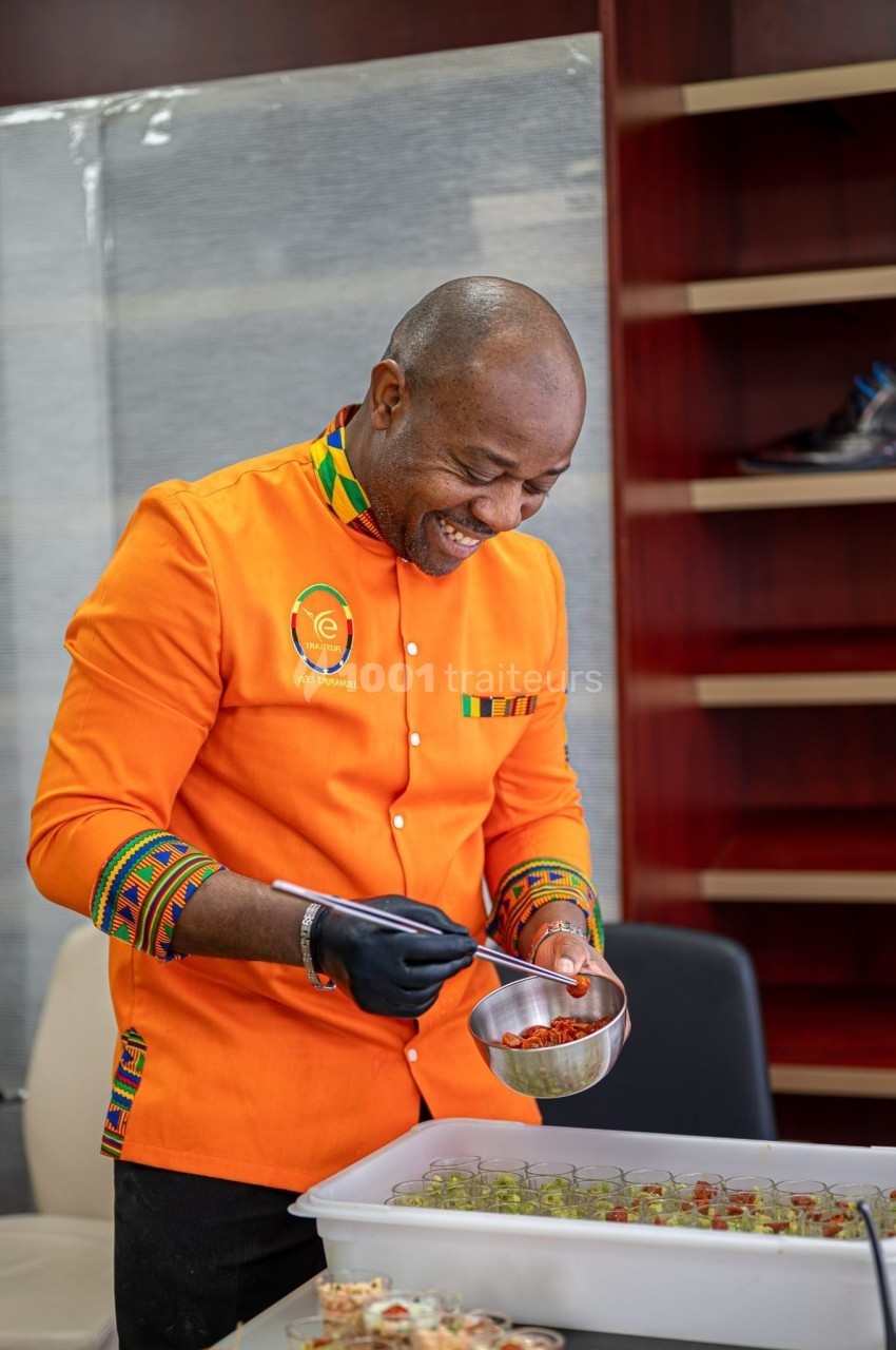 Un chef en veste orange prépare des plats en disposant des ingrédients dans de petits contenants.