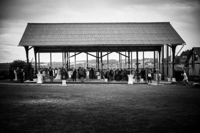 Salle de bain moderne avec douche vitrée, lavabo blanc, miroir, sèche-serviettes et poutres en bois apparentes.