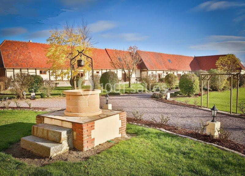 Cour avec un puits en pierre au premier plan, entourée de pelouses, arbustes et bâtiments aux toits rouges.