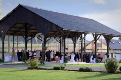 Salle de bain moderne avec douche vitrée, lavabo blanc, miroir, sèche-serviettes et poutres en bois apparentes.