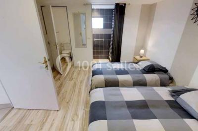 Salle de bain moderne avec douche vitrée, lavabo blanc, miroir, sèche-serviettes et poutres en bois apparentes.